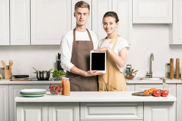 Joven pareja celebración tableta con pantalla en blanco en la cocina - foto de stock