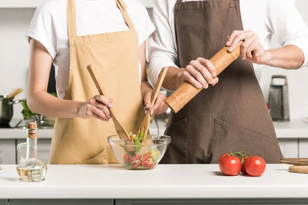 Cropped image of young couple cooking salad in kitchen — Stock Photo