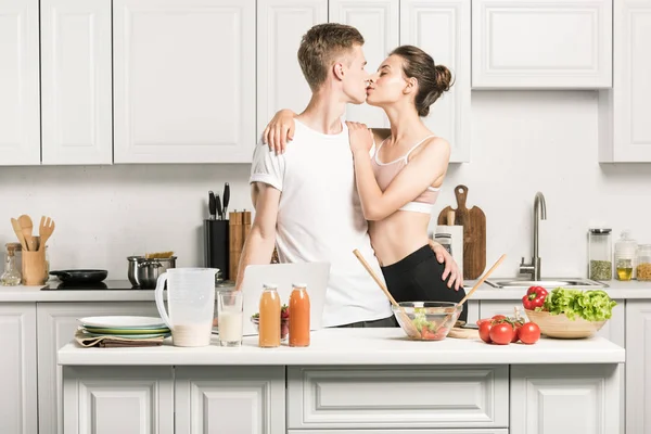 Jovem casal beijando enquanto cozinha salada na cozinha — Fotografia de Stock