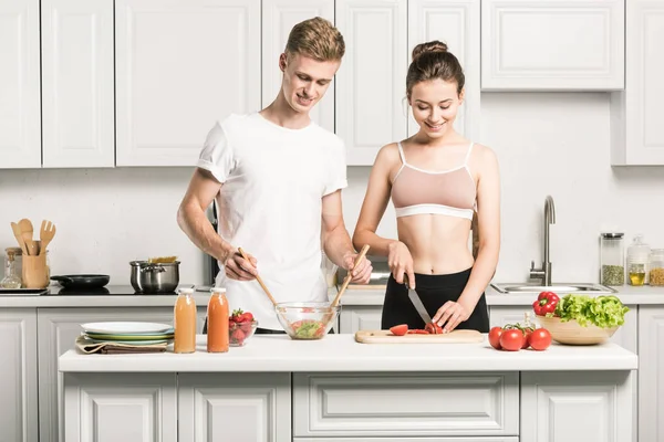 Jovem casal cozinhar salada juntos na cozinha — Fotografia de Stock