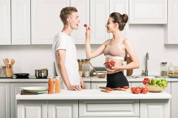 Girlfriend feeding boyfriend with strawberry in kitchen — Stock Photo