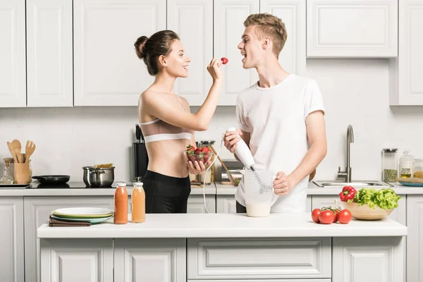 Petite amie alimentation copain avec fraise dans la cuisine — Photo de stock