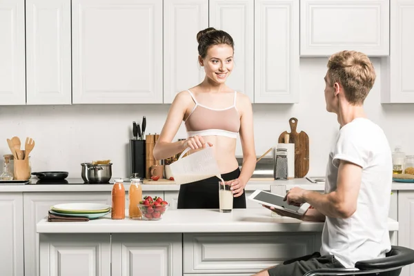 Petite amie verser du lait et petit ami en utilisant une tablette dans la cuisine — Photo de stock