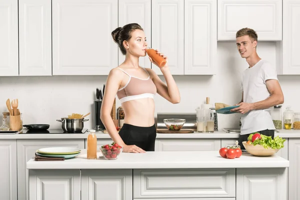 Chica joven en sujetador deportivo beber jugo saludable en la cocina - foto de stock