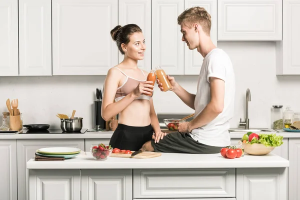 Jovem casal clinking com garrafas de suco saudável na cozinha — Fotografia de Stock