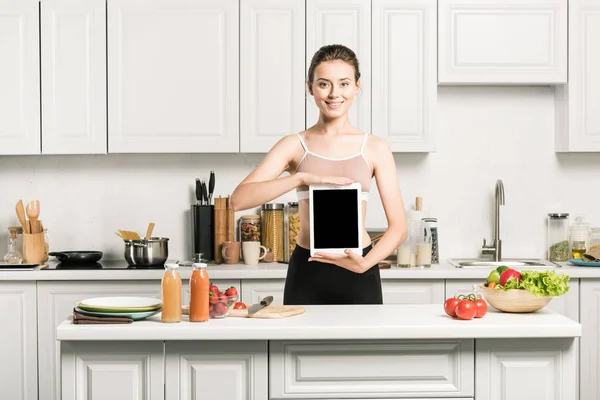 Attraktives Mädchen im Sport-BH hält Tablet mit leerem Bildschirm in der Küche — Stockfoto