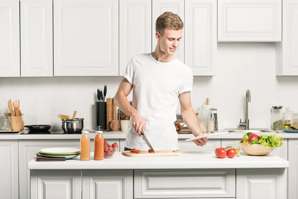 Schöner junger Mann kocht und liest Rezept auf Tablet in Küche — Stockfoto