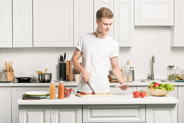 Joven guapo cocina y lectura receta en la tableta en la cocina - foto de stock