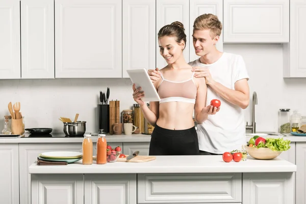 Jeune couple lecture recette pour une alimentation saine sur tablette dans la cuisine — Photo de stock