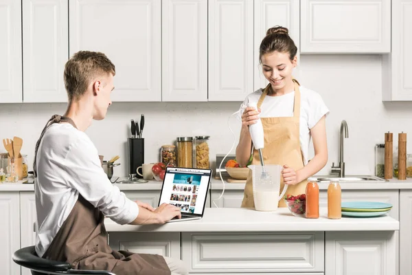 Novia cocina y novio usando el ordenador portátil con página amazon cargado en la cocina - foto de stock