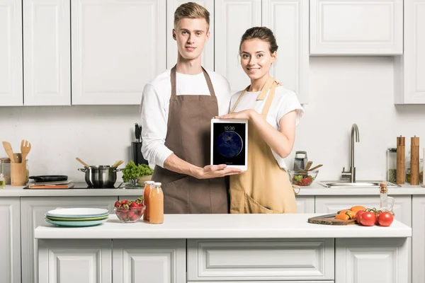 Young couple holding ipad and looking at camera in kitchen — Stock Photo