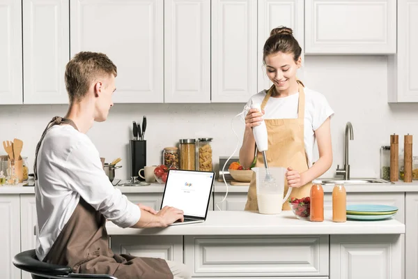 Namorada cozinhar e namorado usando laptop com página do google carregado na cozinha — Fotografia de Stock