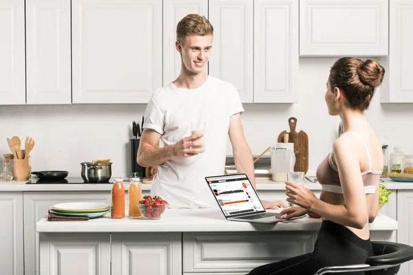Girlfriend using laptop with loaded soundcloud page and looking at boyfriend in kitchen — Stock Photo