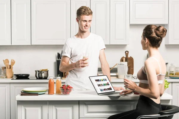 Girlfriend using laptop with loaded youtube page and looking at boyfriend in kitchen — Stock Photo