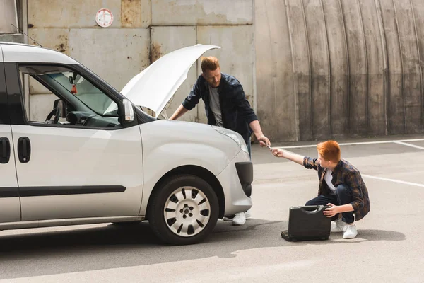 Side view of ginger hair son giving tool for repairing car to father — Stock Photo