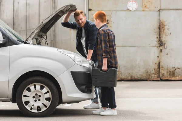 Side view of father and son repairing car with open hood on weekend — Stock Photo
