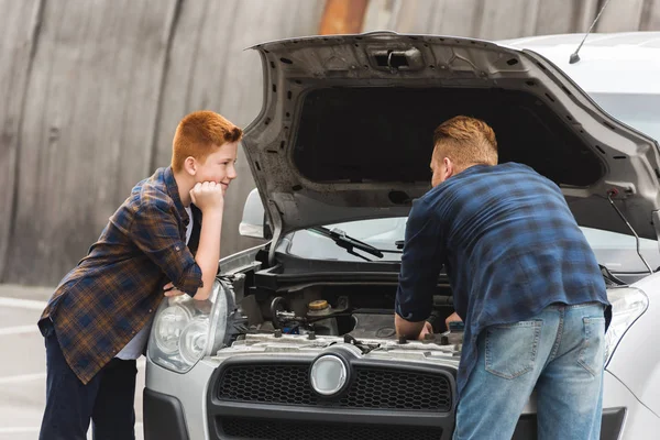 Figlio pensieroso cercando come padre riparazione auto con cappuccio aperto — Foto stock