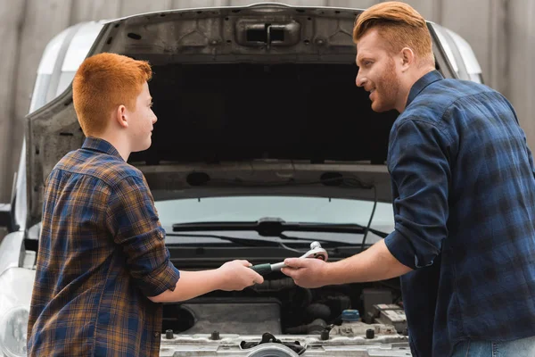 Preteen son giving tool for repairing car to father — Stock Photo