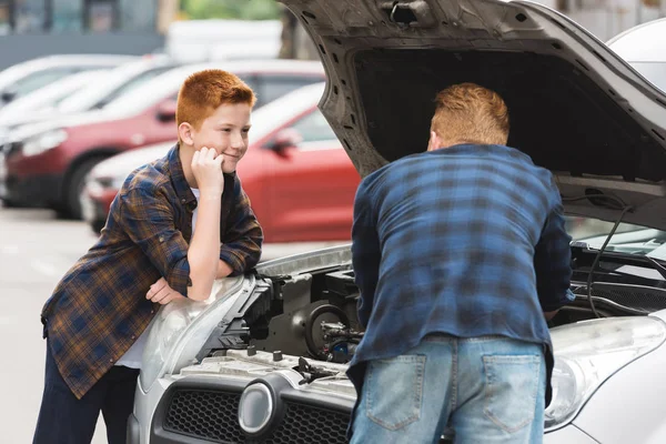 Hijo mirando cómo padre reparación de coche con capucha abierta - foto de stock