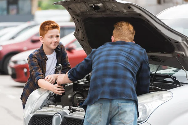 Filho dando ferramenta para reparar carro para o pai — Fotografia de Stock