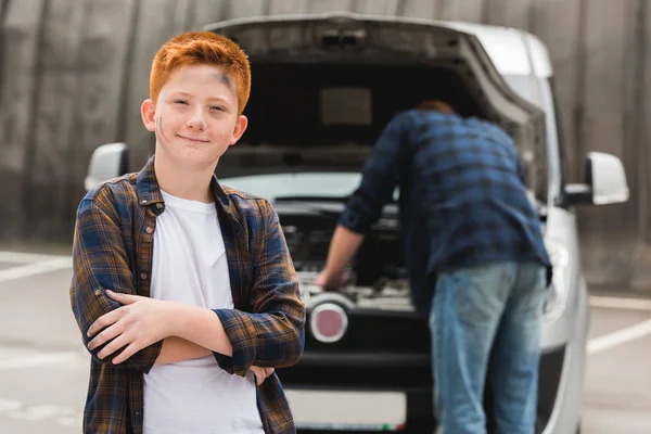 Padre reparación de coche con capucha abierta, hijo mirando a la cámara - foto de stock