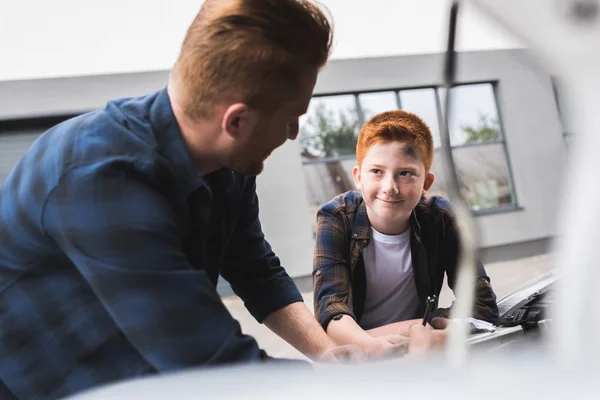 Father and son repairing car with open hood and looking at each other — Stock Photo