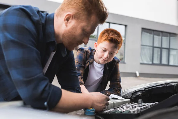 Father and son repairing car with open hood and looking at broken part — Stock Photo