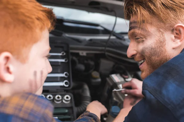 Happy father and son repairing car with open hood and looking at each other — Stock Photo