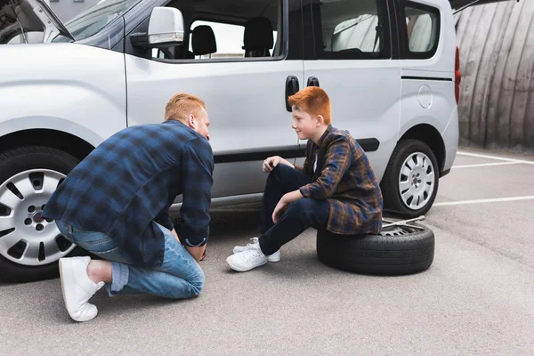 Padre sollevamento auto con martinetto per cambiare pneumatico e guardando il figlio — Foto stock