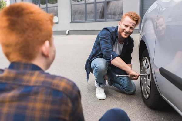 Padre cambiare pneumatico in auto con chiave a ruota e guardando il figlio — Foto stock