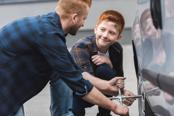 Gengibre cabelo pai e filho mudando pneu no carro com chave de rodas — Fotografia de Stock