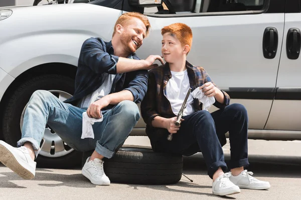 Sonriente padre limpieza hijo cara después de reparar el coche - foto de stock