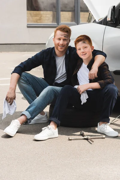 Happy father hugging son after repairing car and they sitting near auto — Stock Photo