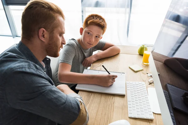 Seitenansicht von Vater hilft Sohn bei Hausaufgaben zu Hause — Stockfoto