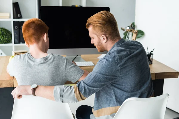 Vista trasera del padre ayudando a su hijo a hacer la tarea en casa - foto de stock