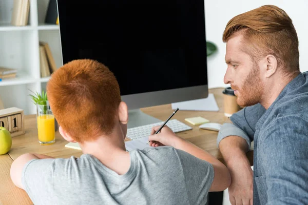 Father helping ginger hair son doing homework at home — Stock Photo