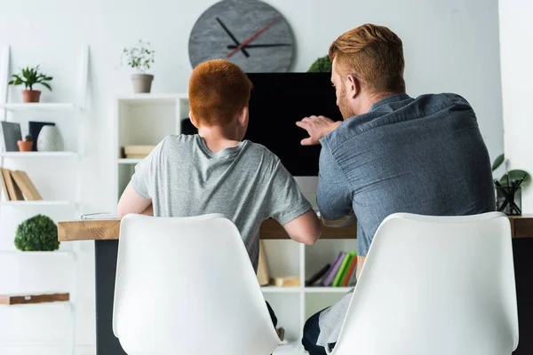 Vista posteriore del padre che aiuta il figlio a fare i compiti a casa e che indica sul computer — Foto stock