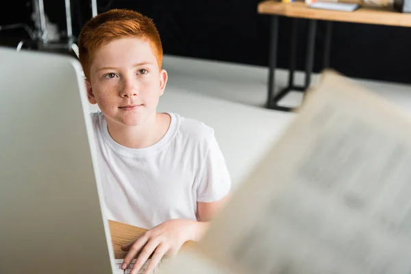 Boy sitting at table with computer and looking away at home — Stock Photo