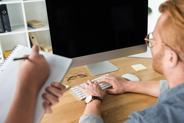 Abgeschnittenes Bild von Vater mit Computer, Sohn mit Stift und Notizbuch zu Hause — Stockfoto