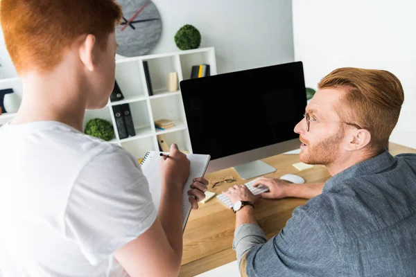 Padre usando la computadora, el hijo que sostiene la pluma y el cuaderno en casa - foto de stock