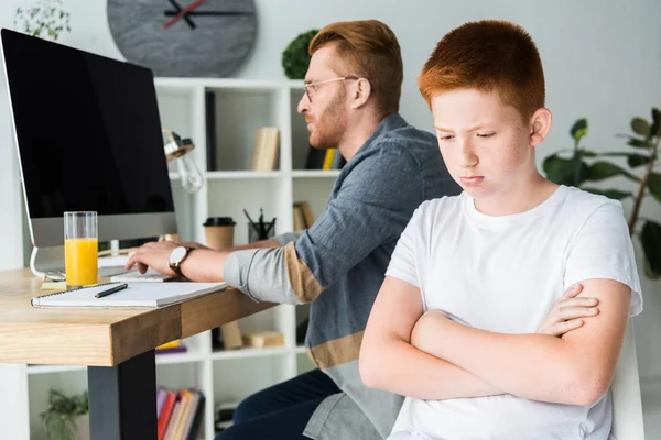 Padre usando la computadora y triste hijo mirando hacia abajo en casa - foto de stock