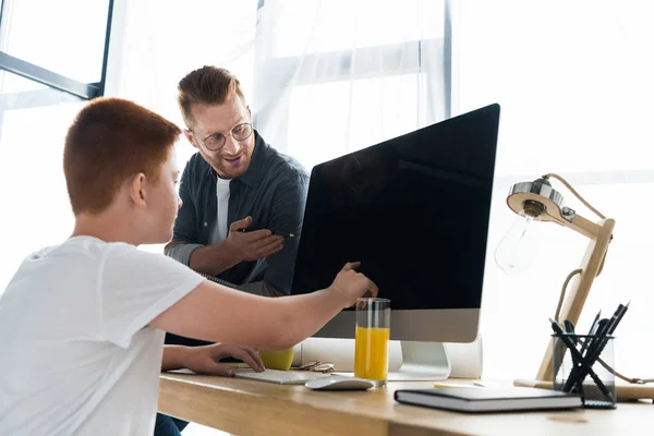 Son pointing on something at computer to father at home — Stock Photo