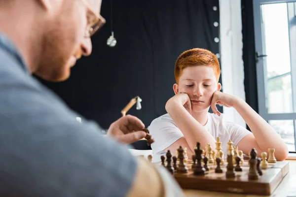 Nachdenklicher Sohn schaut zu Hause auf Schachbrett — Stockfoto