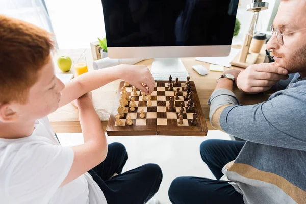 Father and son playing chess at table with computer at home — Stock Photo