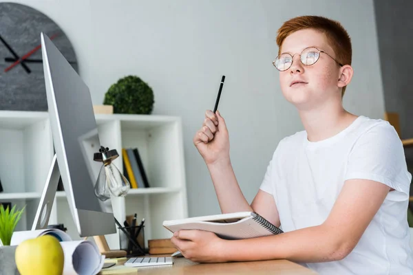 Pensivo preteen gengibre cabelo menino segurando caneta e notebook em casa — Fotografia de Stock