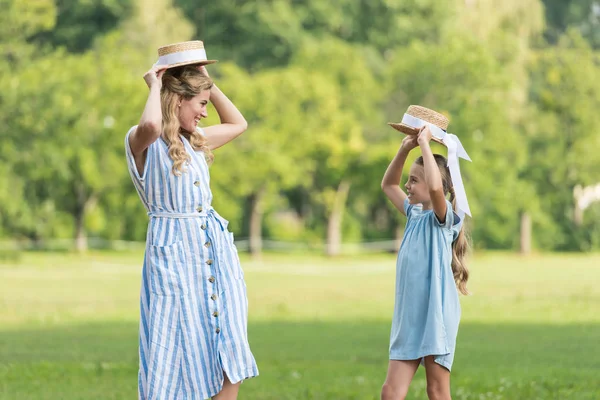 Allegra madre e figlia in posa con cappelli di paglia e guardando l'un l'altro sul prato — Foto stock