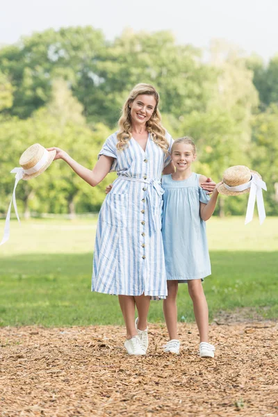 Beautiful mother and adorable daughter posing with straw hats — Stock Photo