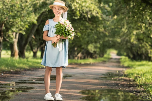 Preteen child in trendy dress and straw hat holding flowers in park — Stock Photo