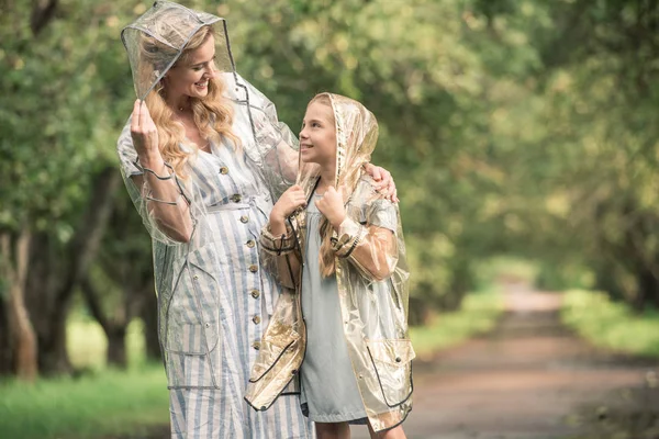 Bela mãe e filha em capas impermeáveis transparentes no parque — Fotografia de Stock