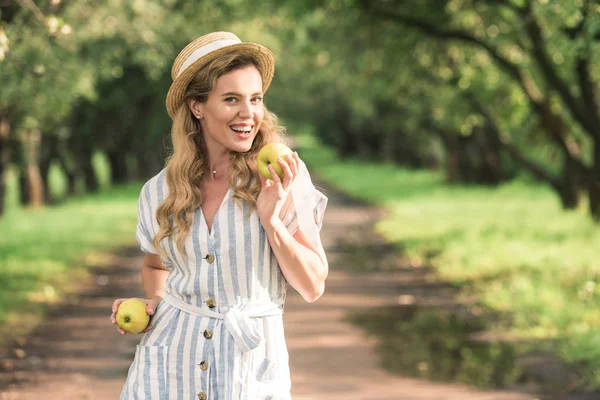 Beautiful stylish woman in straw hat holding two apples in orchard — Stock Photo